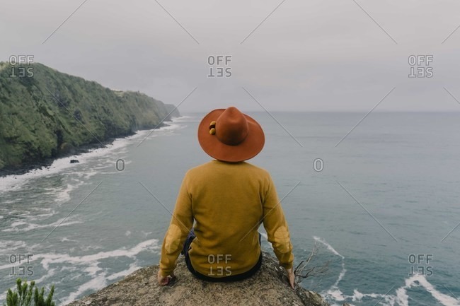 Rear view of man sitting on a rock at the coast on Sao Miguel Island- Azores- Portugal