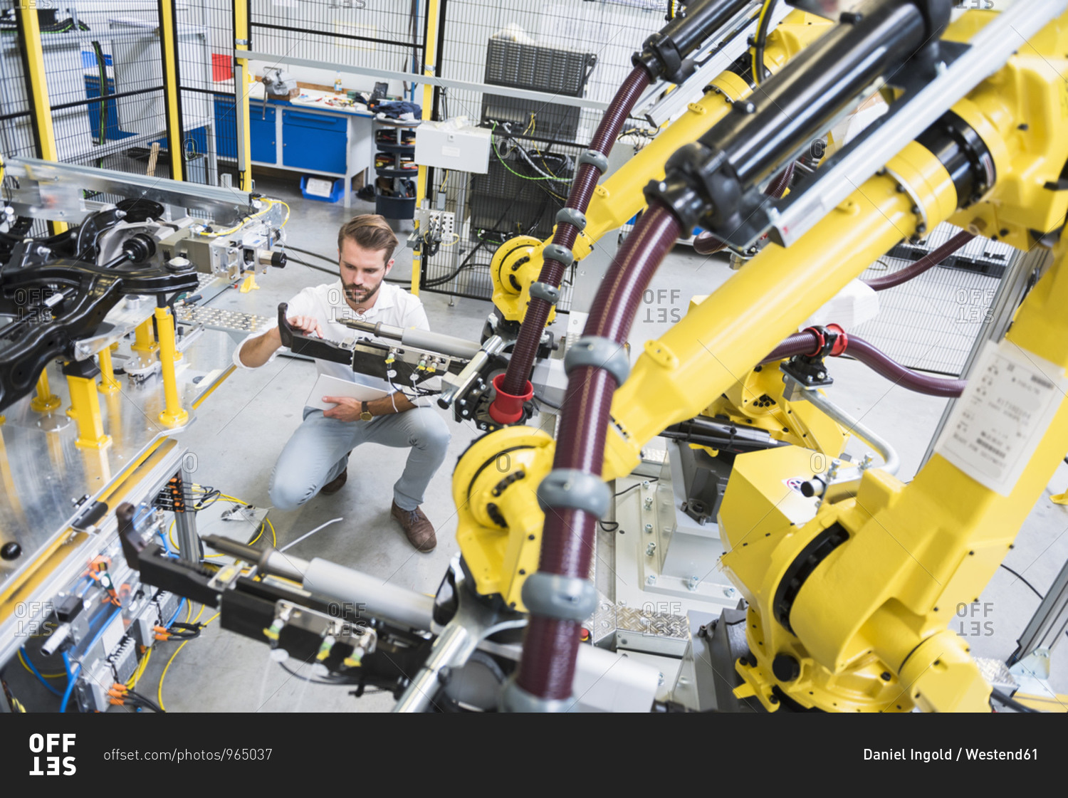 Full length of young engineer crouching while examining computer-aided machinery in automated industry