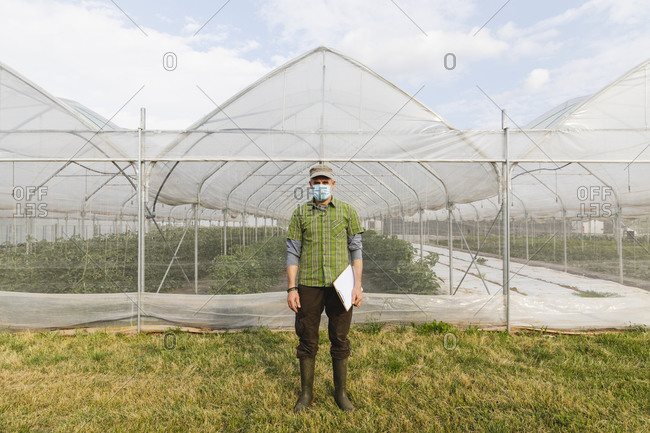 Farmer with mask in front of the organic greenhouse
