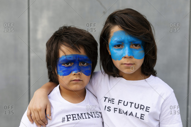 Portrait of two brothers with painted blue masks on their faces wearing t-shirts with feministic imprints