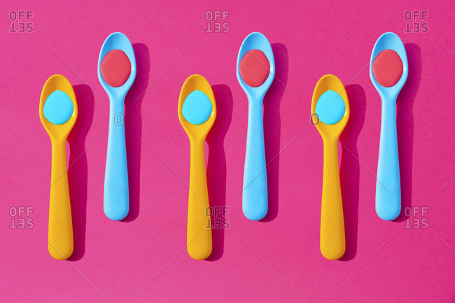 Pattern of yellow and blue plastic teaspoons with blue and red liquid