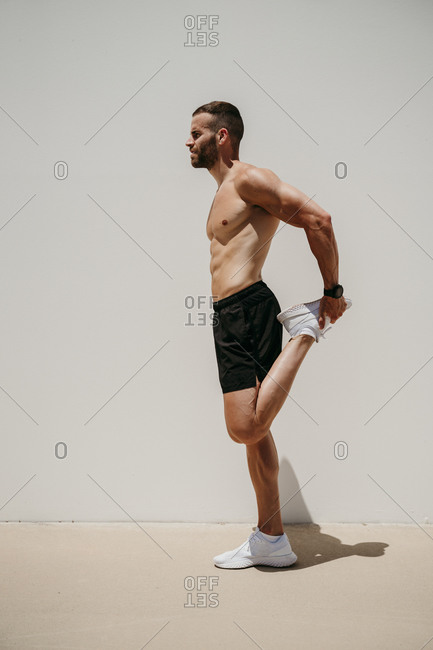 Bare-chested male athlete stretching in sunshine