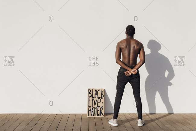 Black man crossing hands behind his back with Black Lives Matter sign leaning on wall