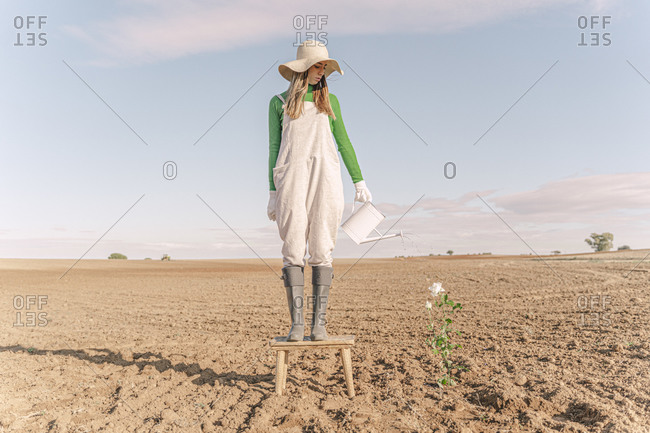 Woman standing on stool- watering flower on barren field