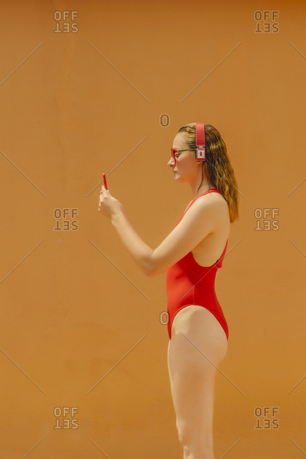 Woman wearing red swimsuit listening music with red headphones while starring at red mobile phone