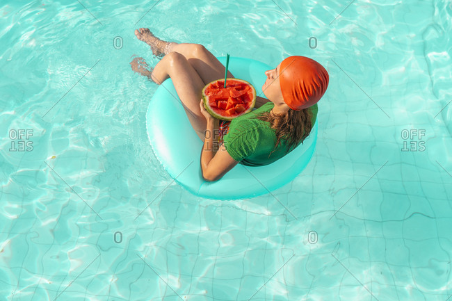 Woman with floating tire and watermelon relaxing in swimming pool