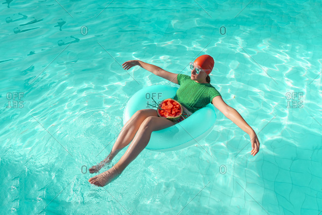Woman with floating tire and watermelon in swimming pool