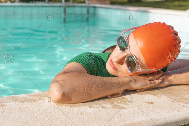 Portrait of woman wearing red swimming cap and sunglasses leaning on poolside