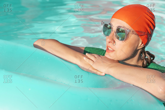 Portrait of woman in pool wearing red swimming cap and mirrored sunglasses leaning on floating tire