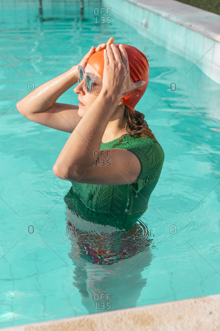 Portrait of woman in swimming pool wearing red swimming cap- green knit pullover and mirrored sunglasses