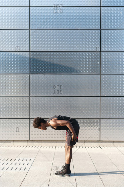 Young man stretching at a metallic shining wall
