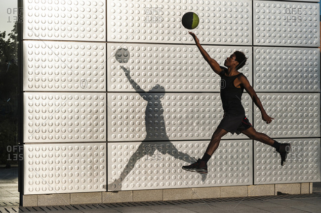 Young man playing basketball at a metallic shining wall
