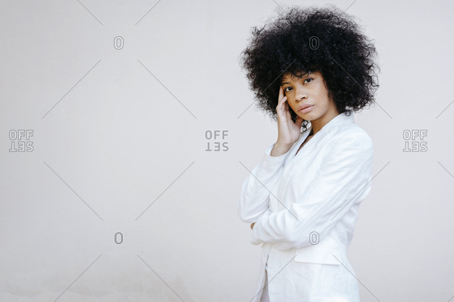 Black woman- wearing white suit- standing in front of white wall- looking pensive