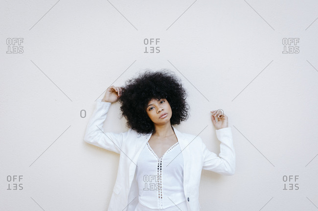 Black woman- wearing white suit- leaning on white wall