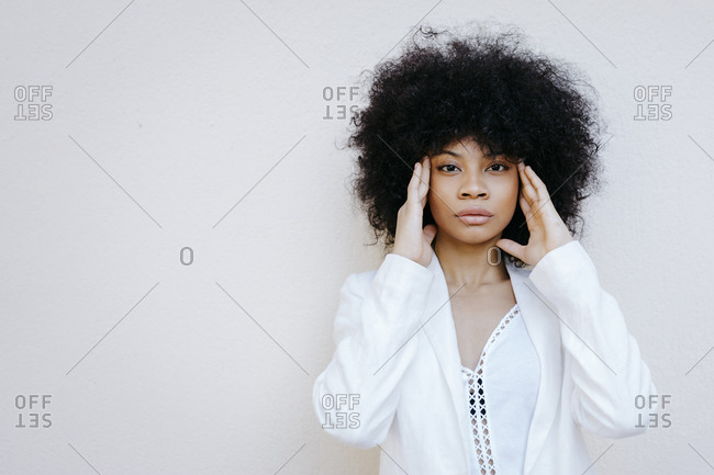 Black woman- wearing white suit- standing in front of white wall- with hands on forehead