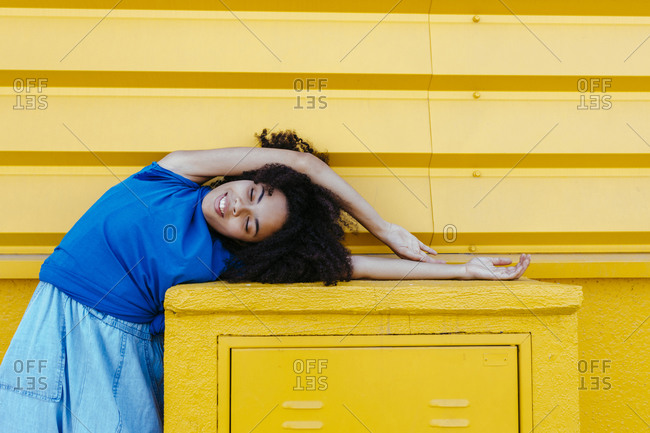 Dreamy woman bending sideways over platform in front of yellow wall