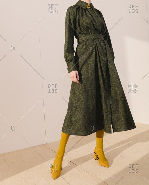Young woman wearing a belted dark green leafy pattern dress with yellow tights and shoes