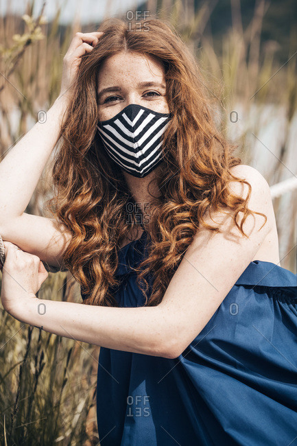 Ginger young woman on the lake with a stiped mask