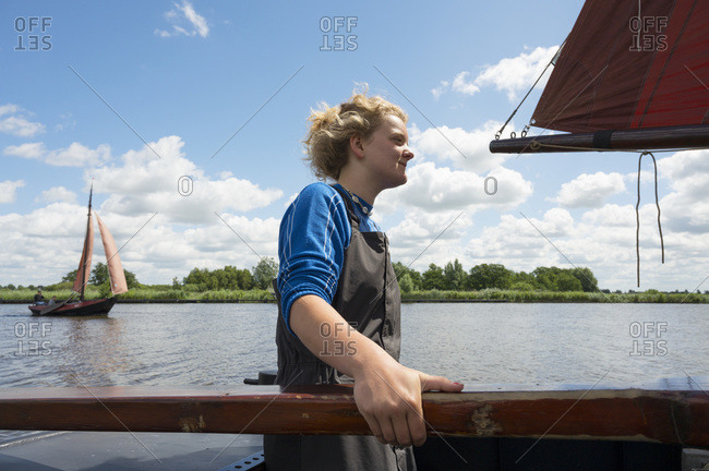 Girl stands at helm of large flat-bottom traditional sailing ship,