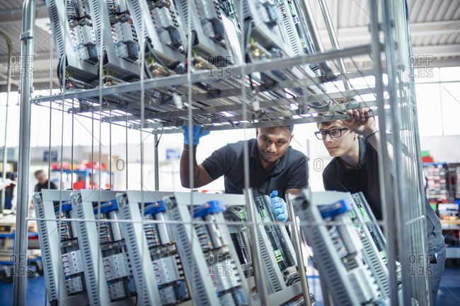 Workers with electronic parts on racks in electronics assembly factory