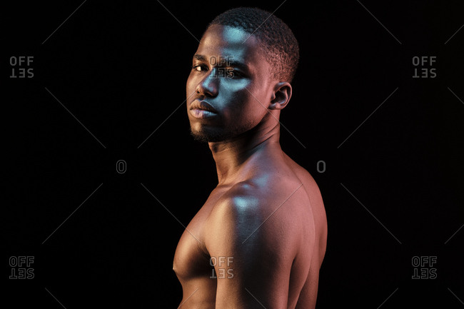 Close up portrait of a black man looking at camera lit with colored lights