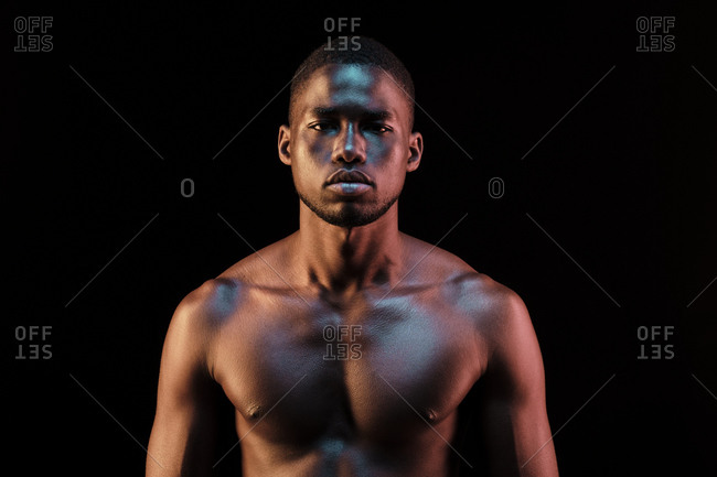 Portrait of a black man looking at camera lit with colored lights shining