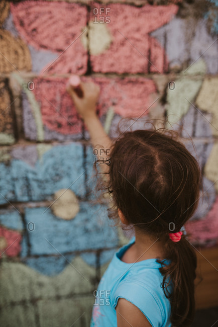 Rear view of little girl coloring a flower with chalk on brick wall