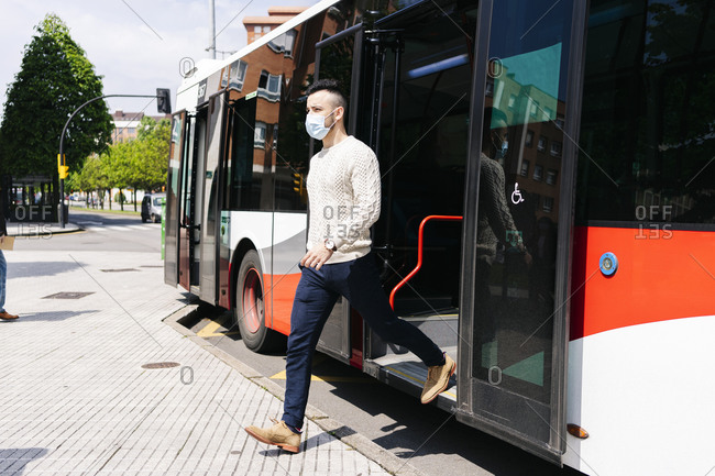 Young man wearing protective mask getting off public bus- Spain
