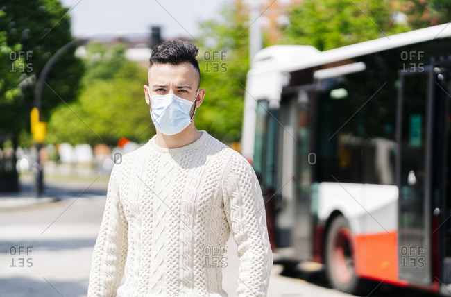 Portrait of young man wearing protective mask waiting at bus stop- Spain