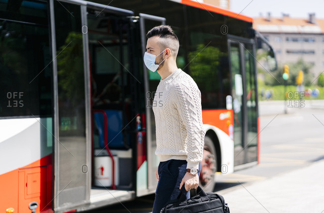 Young man wearing protective mask walking in front of public bus- Spain