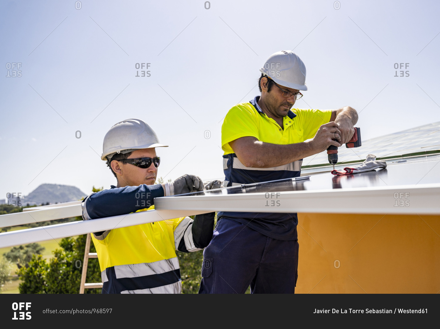 Male technicians installing solar panels on house roof against sky during sunny day