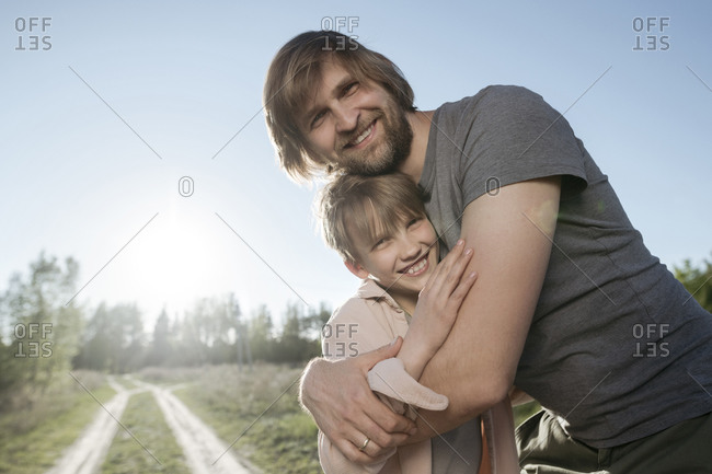 Happy loving father embracing daughter while standing against clear sky in park during sunny day