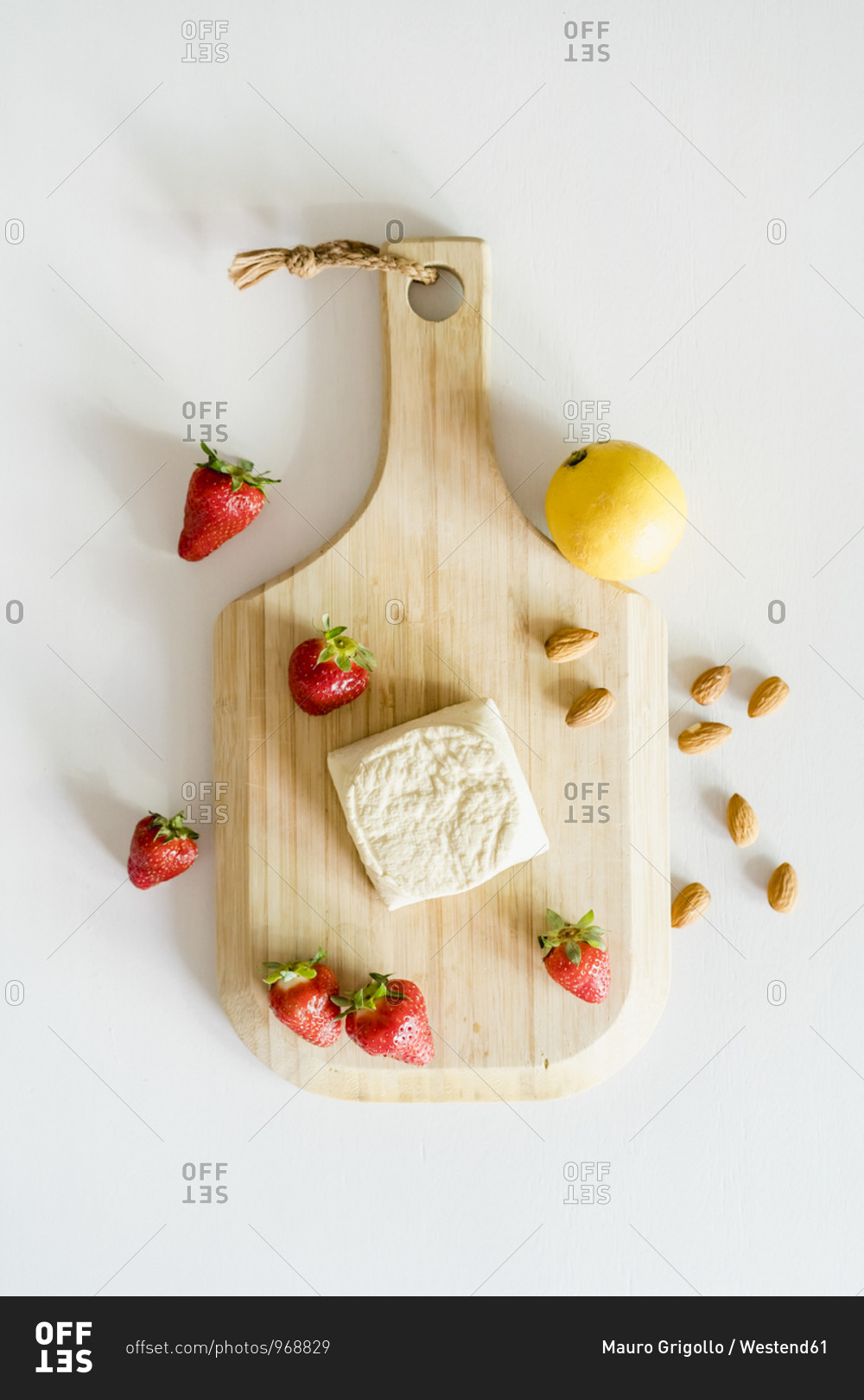 Wooden cutting board- fresh strawberries- almonds- single lemon and homemade vegan cheesecake