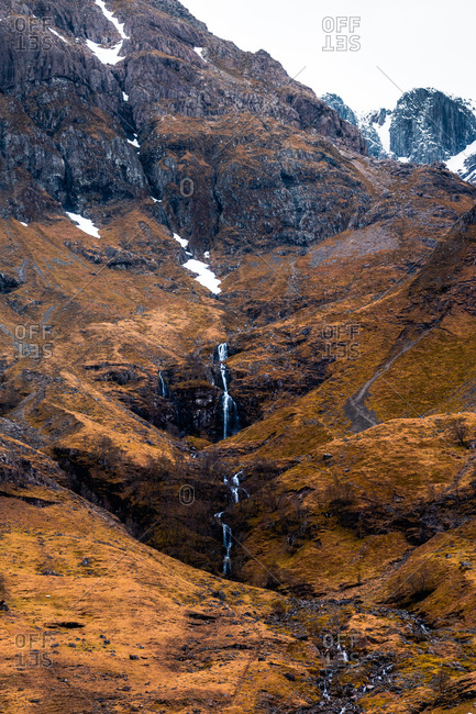 Rough rocky mountain slope with leafless bushes and waterfall in Scottish Highlands