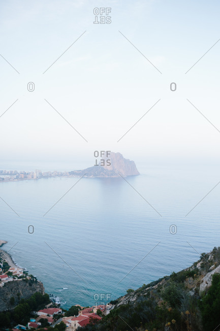 Aerial view of rocky coastline with islet in the middle of the sea close to sea bay with calm blue water against cloudy sky and horizon in light haze at daytime
