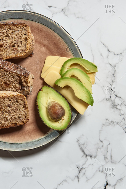 Top view of fresh sliced wholegrain bread served with avocado and cheese for healthy nutrient breakfast on kitchen marble table