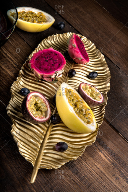Top view of tasty passion fruits and pitaya on gold leaf dish arranged with purple grapes on wooden table
