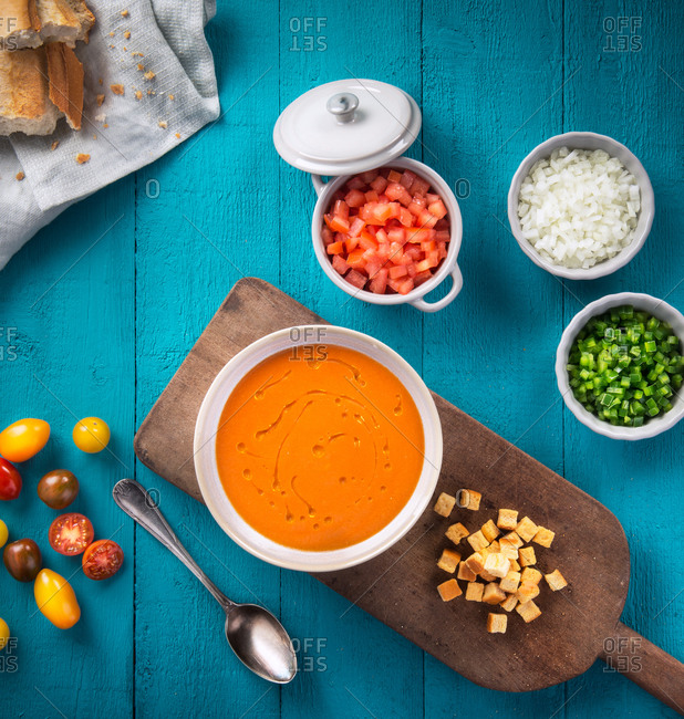 Top view of bowl of Andalusian gazpacho with tasty crackers in composition with fresh chopped vegetables and onion as ingredients on light blue wooden table
