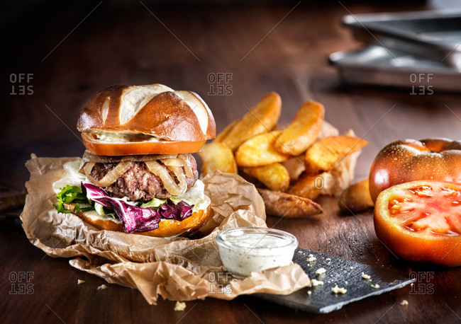 Appetizing big burger with fresh vegetables and beef patty with fried potatoes served on slate board with fries