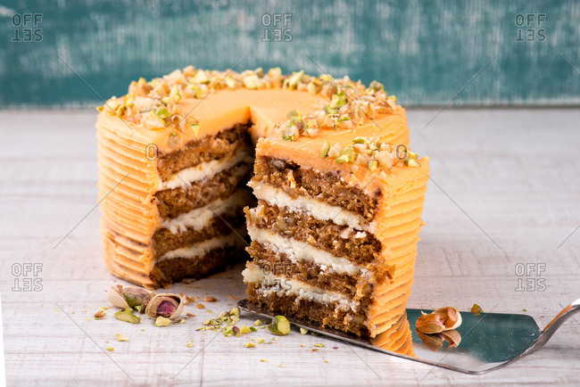 Cake server with piece of delicious carrot cake with pistachios on wooden table