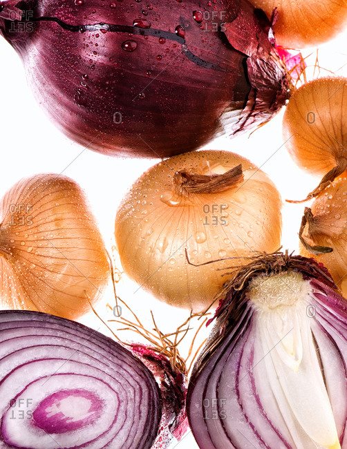 Bunch of fresh whole and sliced red and white onions of various shapes and sizes on white background