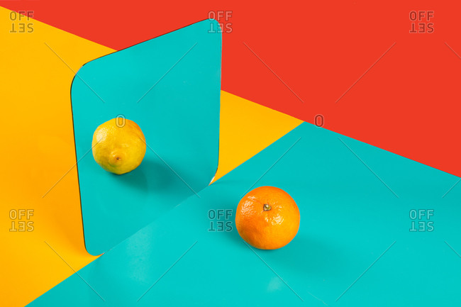 Vibrant background with mirror reflection of fresh orange as lemon on blue surface in composition with empty red and yellow areas like concept of perception in three dimensional space and distortion of imagination