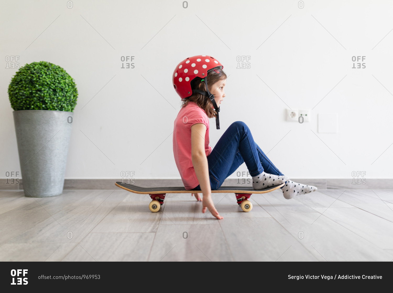 strap major Refinement Little kid in red spotted helmet and casual clothes and dreaming about  outdoors amusement while sitting alone on longboard in corridor of light  modern apartment staying at home stock photo - OFFSET