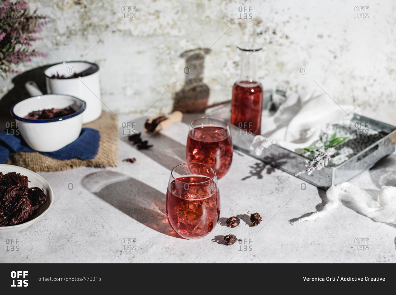 High angle of jar and glasses of delicious natural red hibiscus tea placed near pots with dry flowers on table against shabby wall