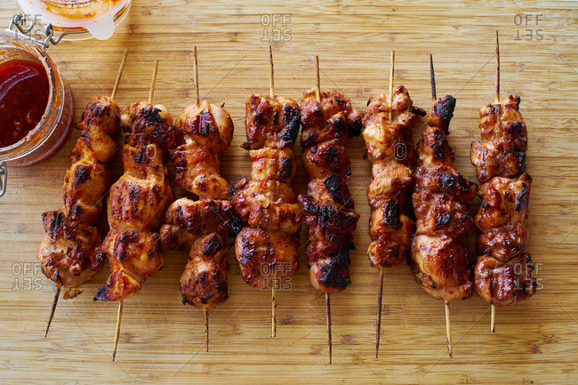 Cooked chicken skewers with spicy sticky glaze on wooden cutting board