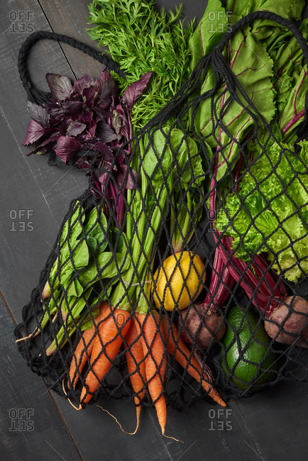 Freshly picked natural organic different greenery and vegetables in an eco-friendly net bag on a dark wooden background, copy space. Top view. Vegetarian healthy food.