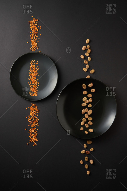 Healthy organic vegetarian food - two lines from natural organic beans and red lentil on two black ceramic plates on the same color background, copy space. Top view. Vegan food concept.