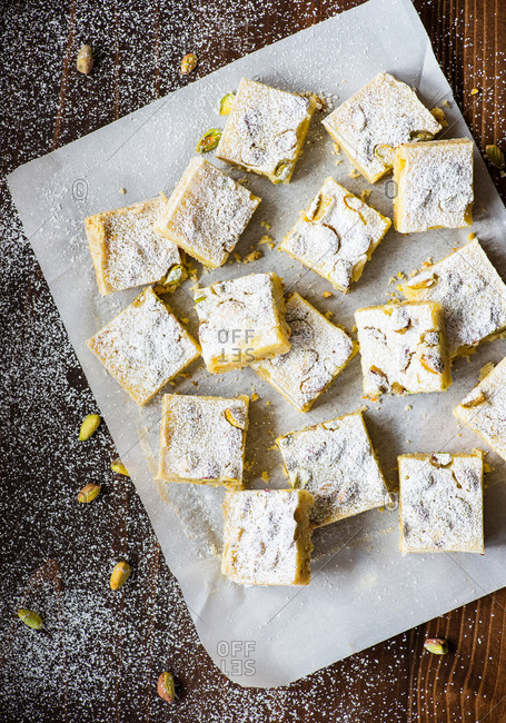 Overhead view of lemon bars with pistachio nuts on parchment paper over dark background