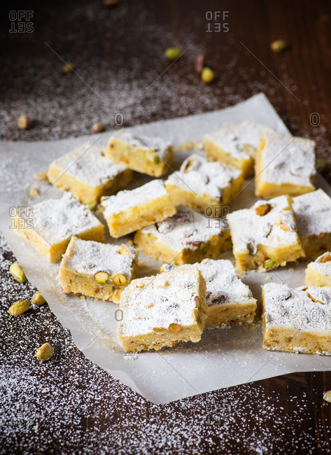 Lemon bars with pistachio nuts on parchment paper over dark background