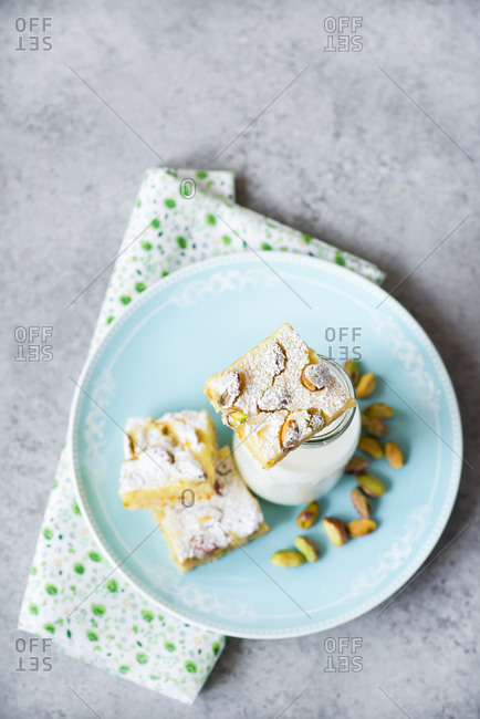 Overhead view of lemon bars with pistachio nuts on plate with bottle of milk on a blue plate and gray background